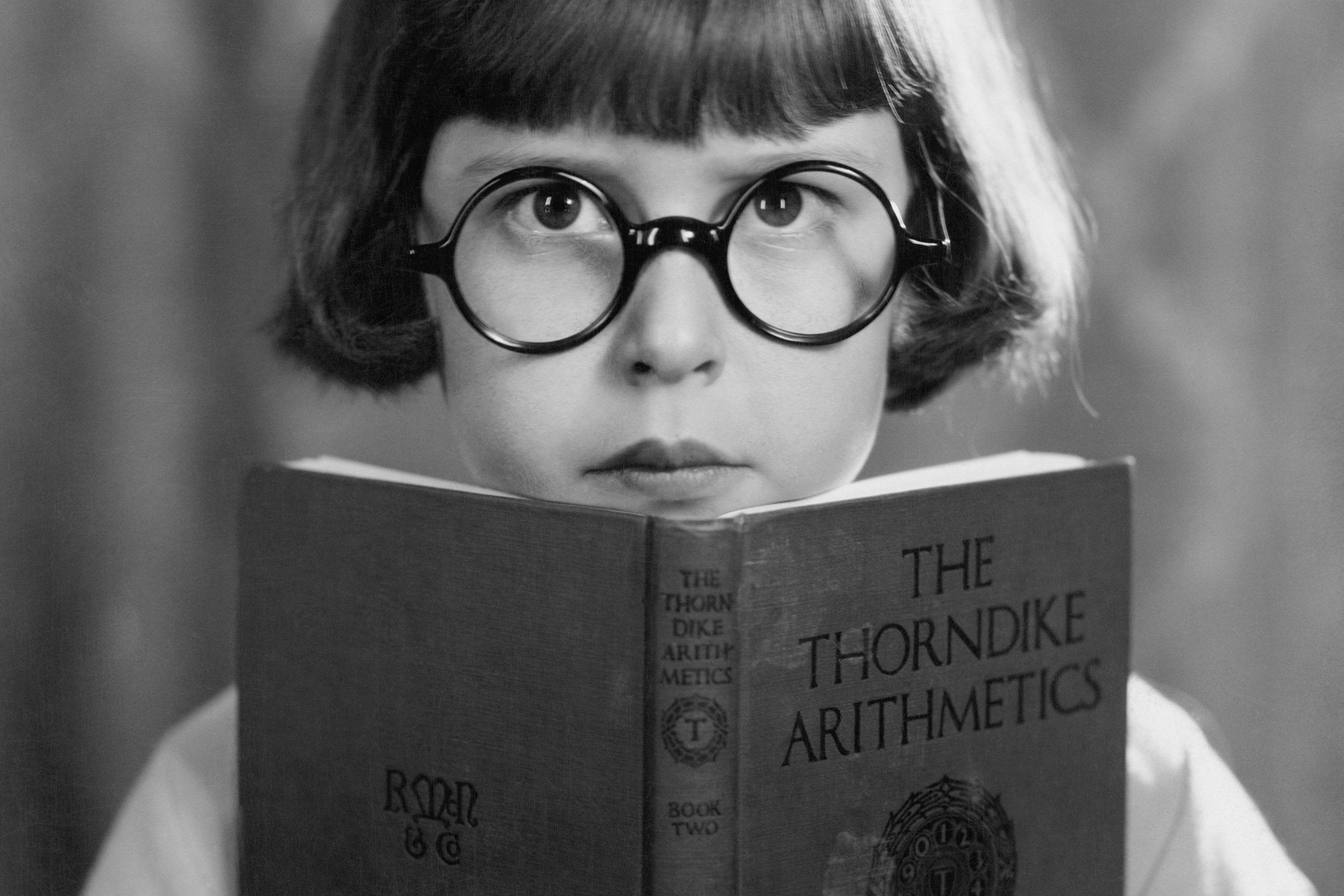 A child wearing oval glasses reads an aritmentic book